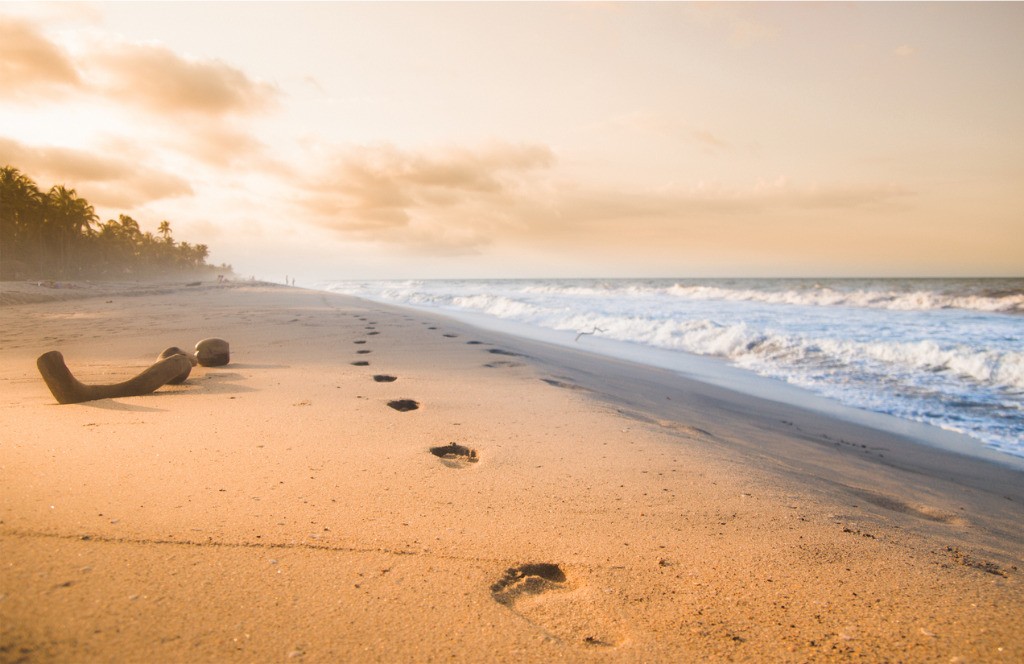 Sanfter Strand bei Sonnenuntergang mit Fußspuren im Sand — ein Bild für den eigenen, achtsamen Weg.