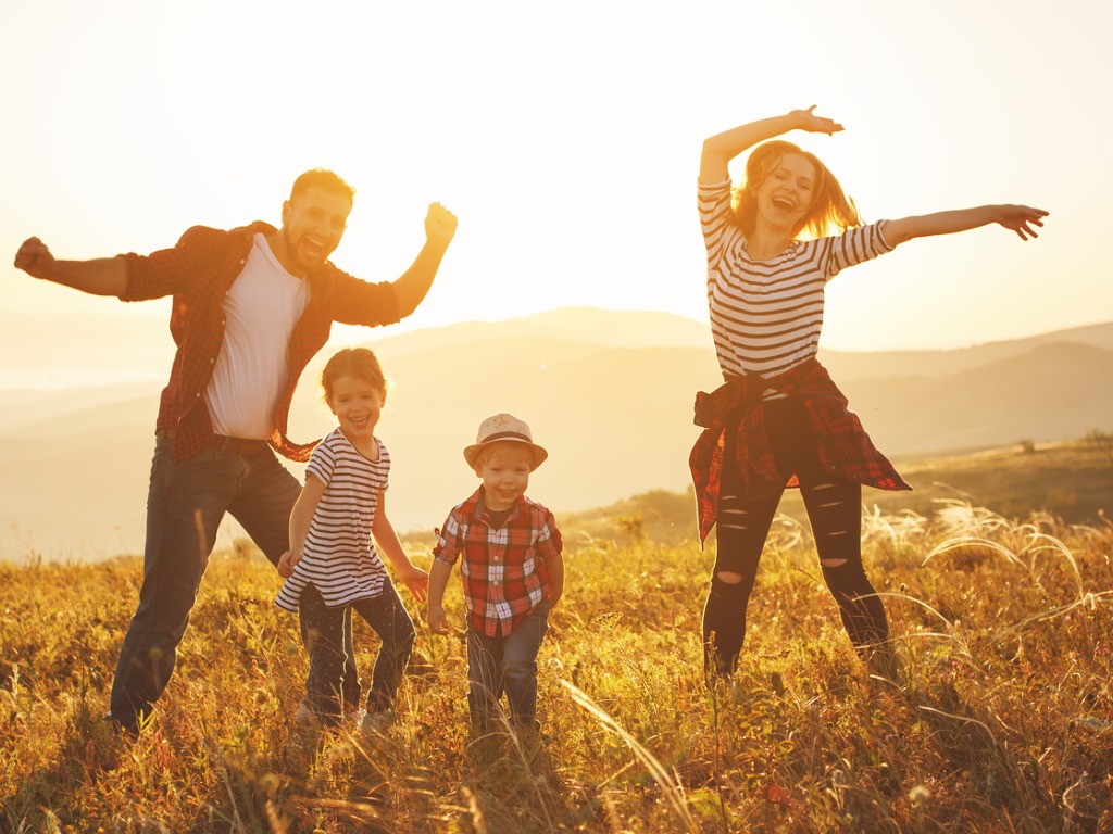 Eine Familie tanzt im warmen Abendlicht auf einer Wiese — Lebensfreude pur.