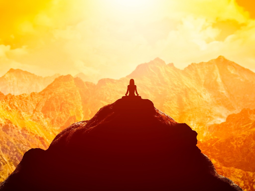 Person in Meditation auf einem Berggipfel im warmen Sonnenlicht.
